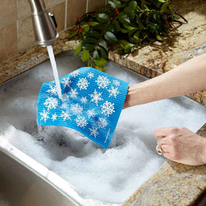Swedish dishcloth with snowflake pattern being run under water over a kitchen sink filled with soapy water