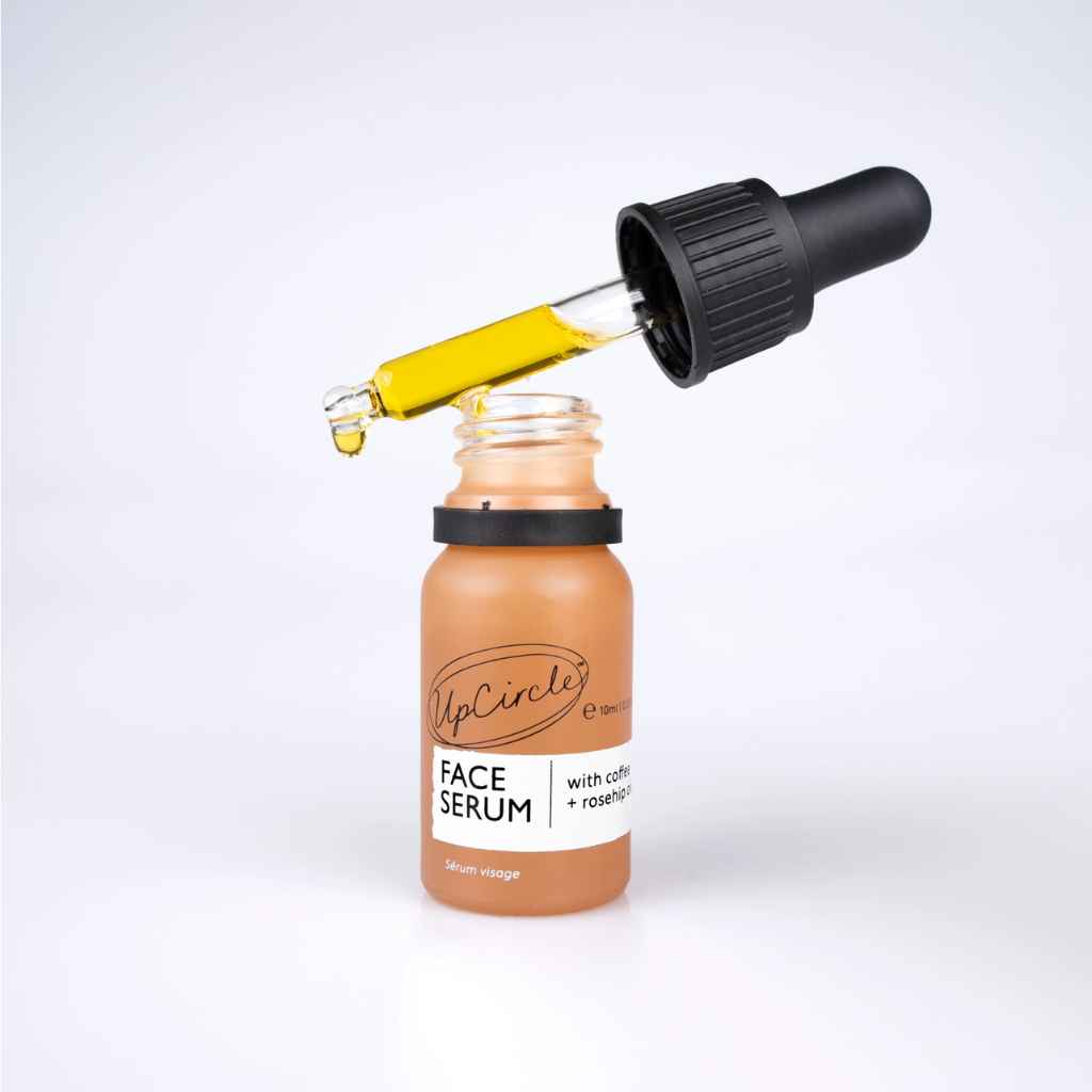 small glass bottle with dropper top, shown open with gold colored oil dripping. UpCircle organic Face Serum 