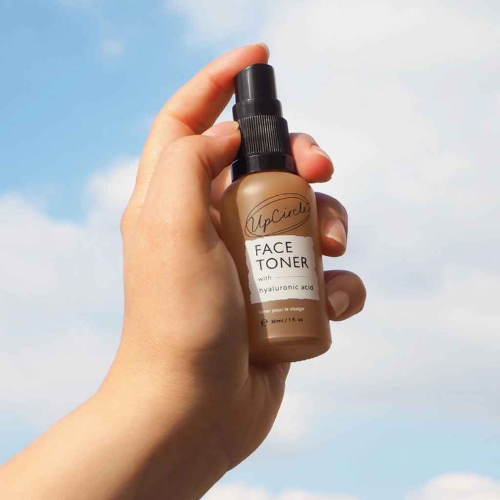 UpCircle Face Toner in travel size glass spray bottle, shown in a person's hand, for scale