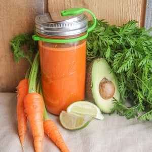 carrots, lime, and avacode slices surrounding mason jar filled with orange colored juice with eco jarz lid and green pop top