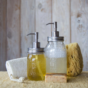 two different sized mason jars with stainless steel dispenser lids. left jar has yellow soap, right jar has clear soap. displayed in front of natural sponges