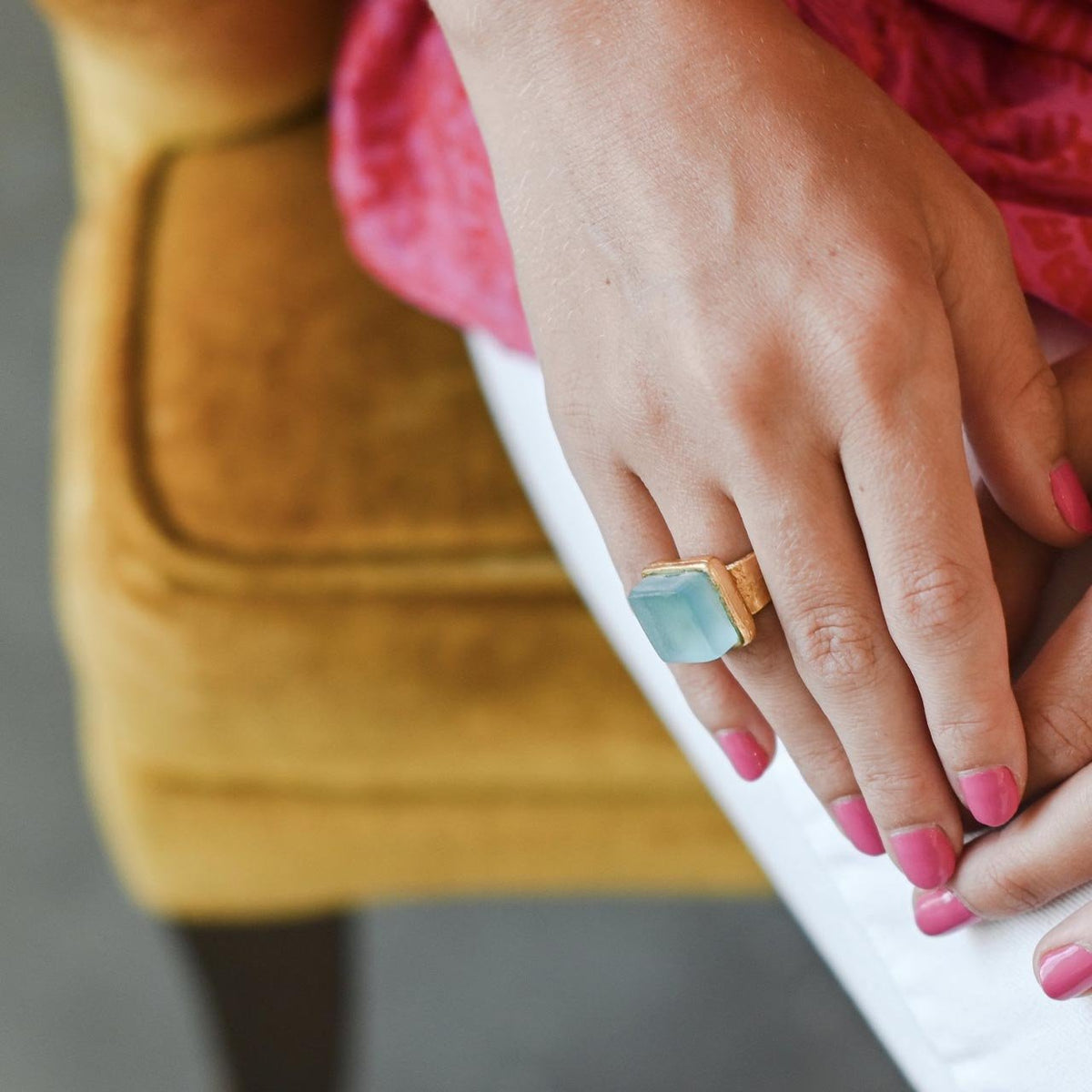 Close up of a light blue recycled glass cocktail ring with a gold band and a square stone on a woman&#39;s hand