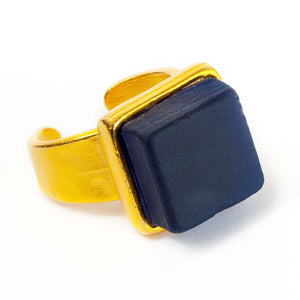 Close up of a dark blue recycled glass cocktail ring with a gold band and a square stone