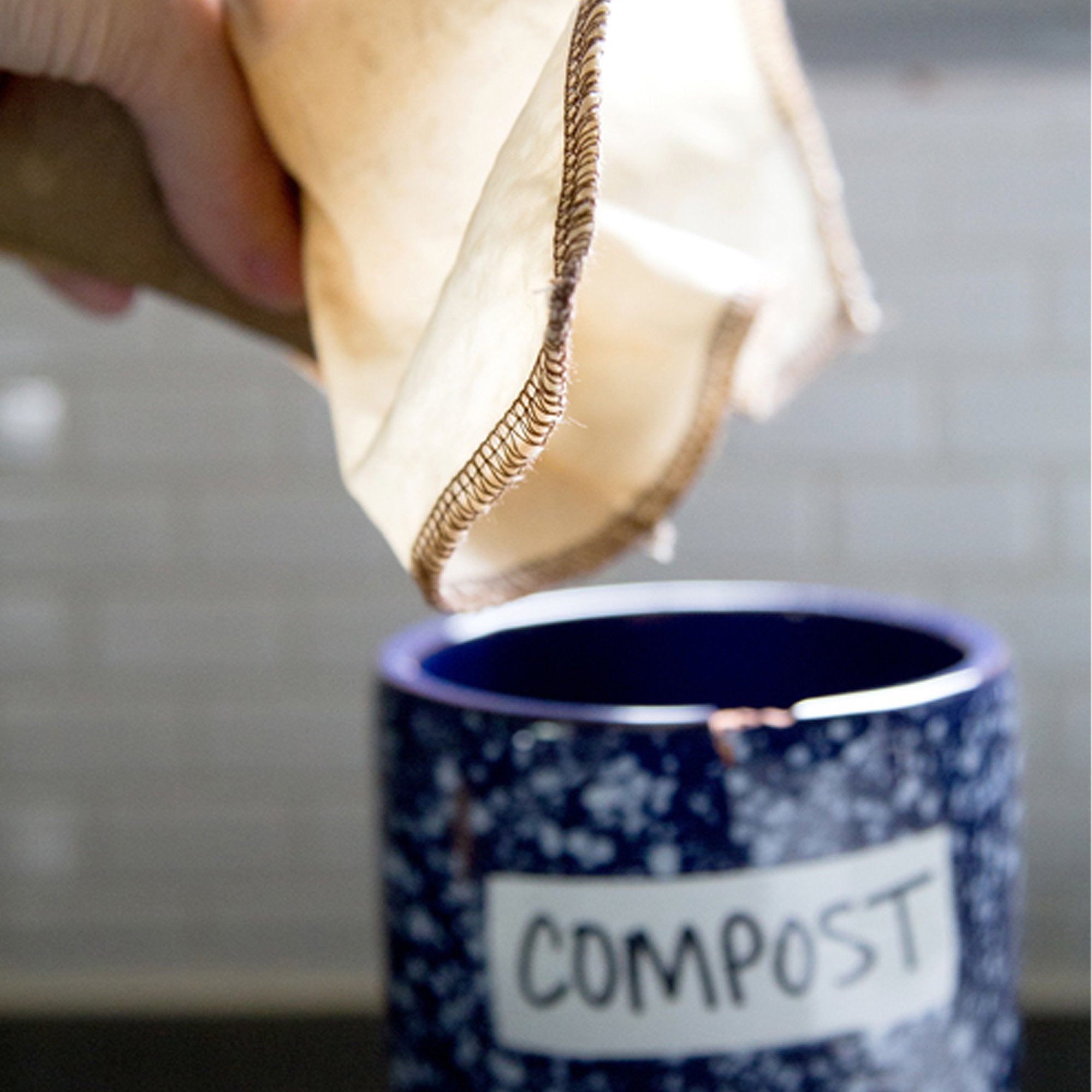 Reusable, organic cotton coffee filters made in the USA. #2 filter size pouring old coffee grounds into blue ceramic labeled compost