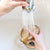 two hands washing reusable coffee filter in sink under faucet