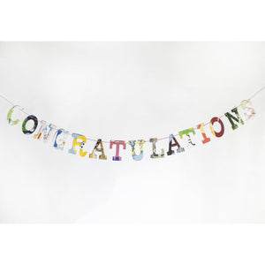 "Congratulations" garland, multi colored collage style, hanging on white wall