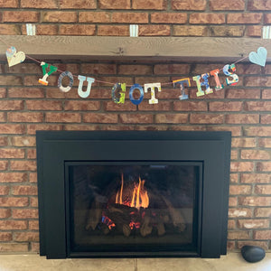 multicolored "you got this" with hearts garland, hanging over brick fireplace indoors