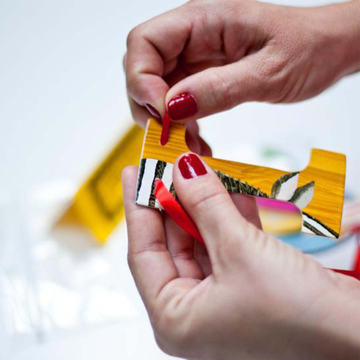 womens hands with red nail polish, threading red ribbon through the letter &quot;I&quot;, constructing a custom garland