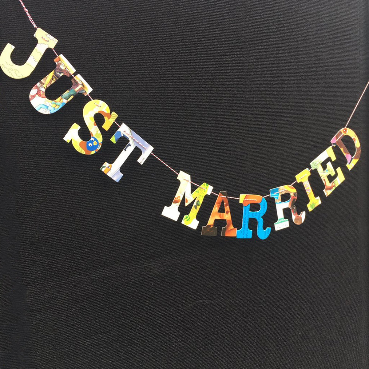 multicolored collage style &quot;Just married&quot; garland, hanging on black canvas