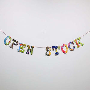 multi-colored, collage style "open stock" garland displayed  hanging on white wall