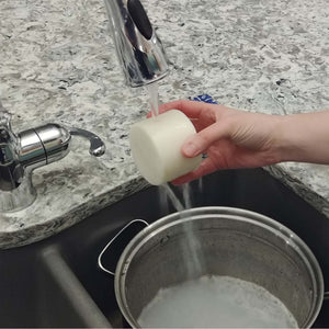 hand holding 7 oz dish soap cylinder under running water in sink, cleaning silver pot 