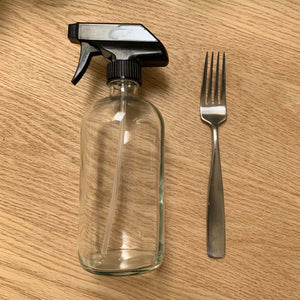clear glass spray bottle with black spray lid, on wood table top next to fork to show scale