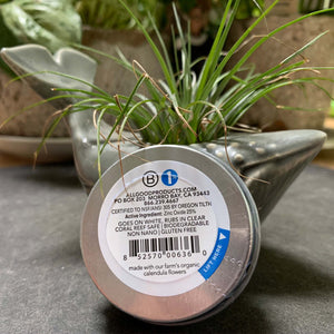 bottom of 1 oz sunscreen butter tin. list of active ingredients and application instructions. leaning on grassy plant in humpback whale shaped vessel 