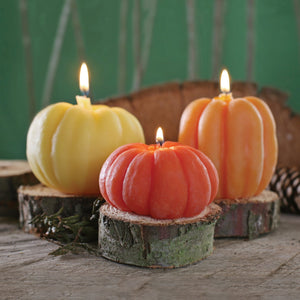 Three pumpkin shaped candles on wood coasters, lit
