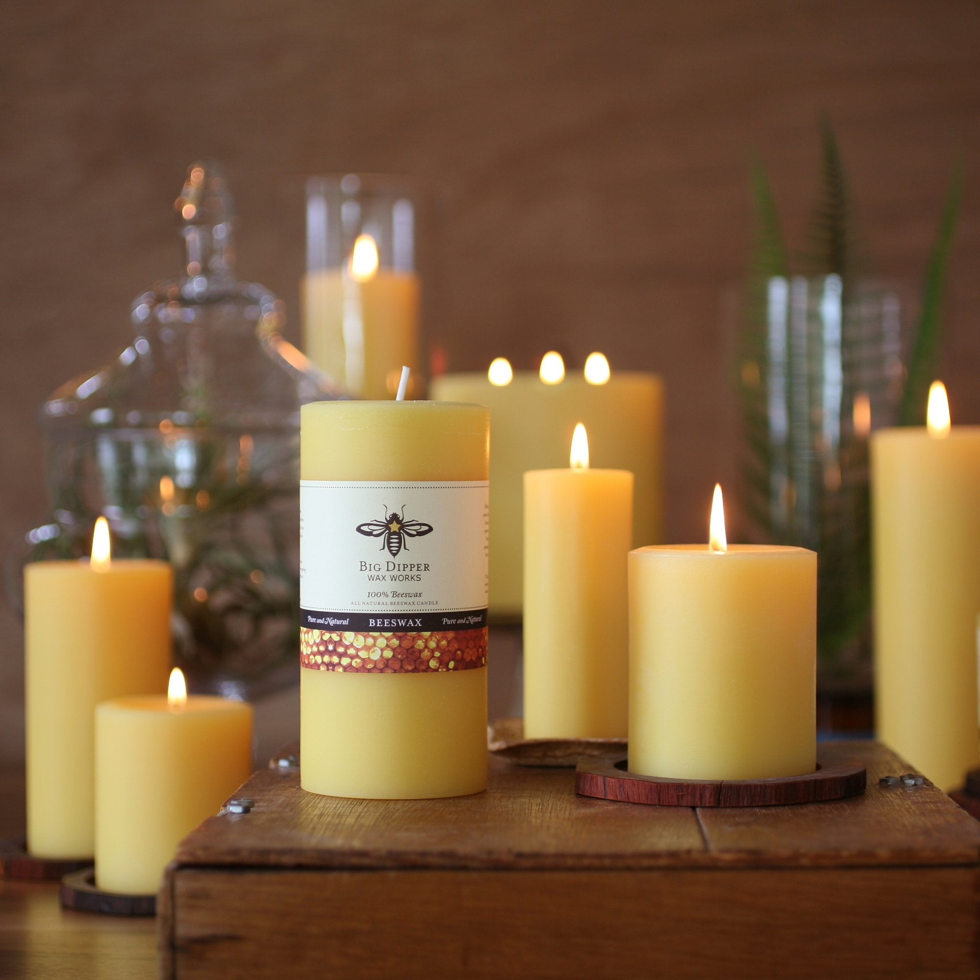 eight golden honey 100% Pure Beeswax Candles of different heights and widths, lit atop on ebony table top including succulents