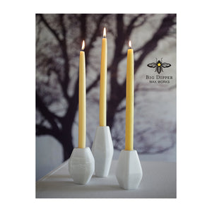 three natural colored 100% Pure Beeswax tapers in white ceramic holders, with winter tree backdrop