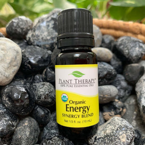 10 ml black bottle with yellow label. organic energy synergy essential oil blend. displayed on assorted rocks