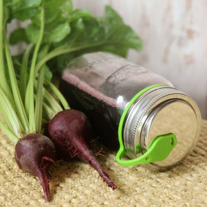 two beets and mason jar on its side filled with beet juice, eco jarz lid and green pop top