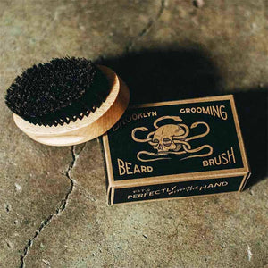 Beechwood brush with boar bristles sitting near black and natural paper box with label for Brooklyn Grooming Beard Brush