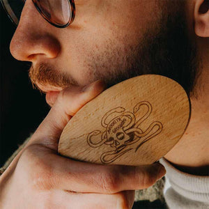 Close-up photo of a man holding a wooden beard brush against his beard